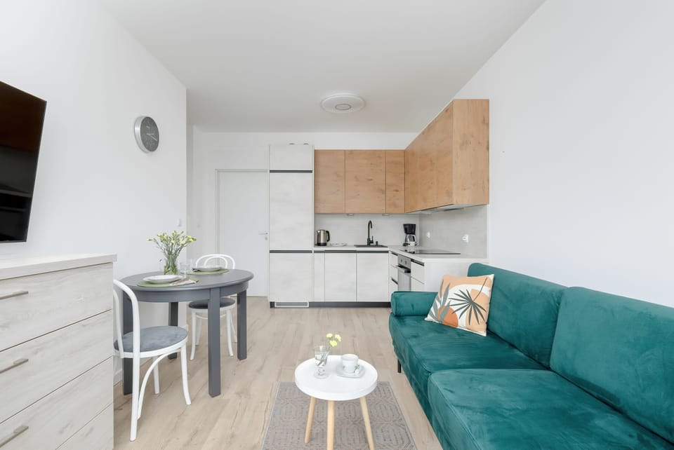 A functional open-plan space with a sofa, dining set, and kitchen. Natural light fills the room through wide windows.