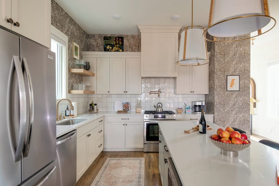 Stainless steel fridge, dishwasher, and gas stove pop among the white cabinets and backsplash