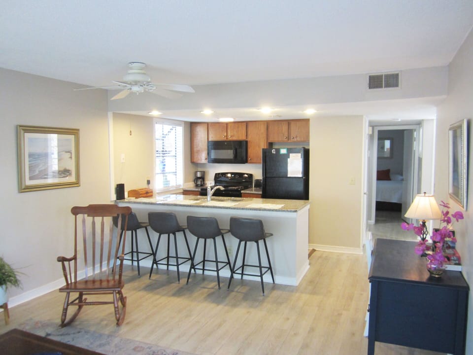 Step into your spacious open-concept living area where warm wood floors flow seamlessly into a modern kitchen with granite countertops and breakfast bar seating—perfect for your morning coffee or casual dining.