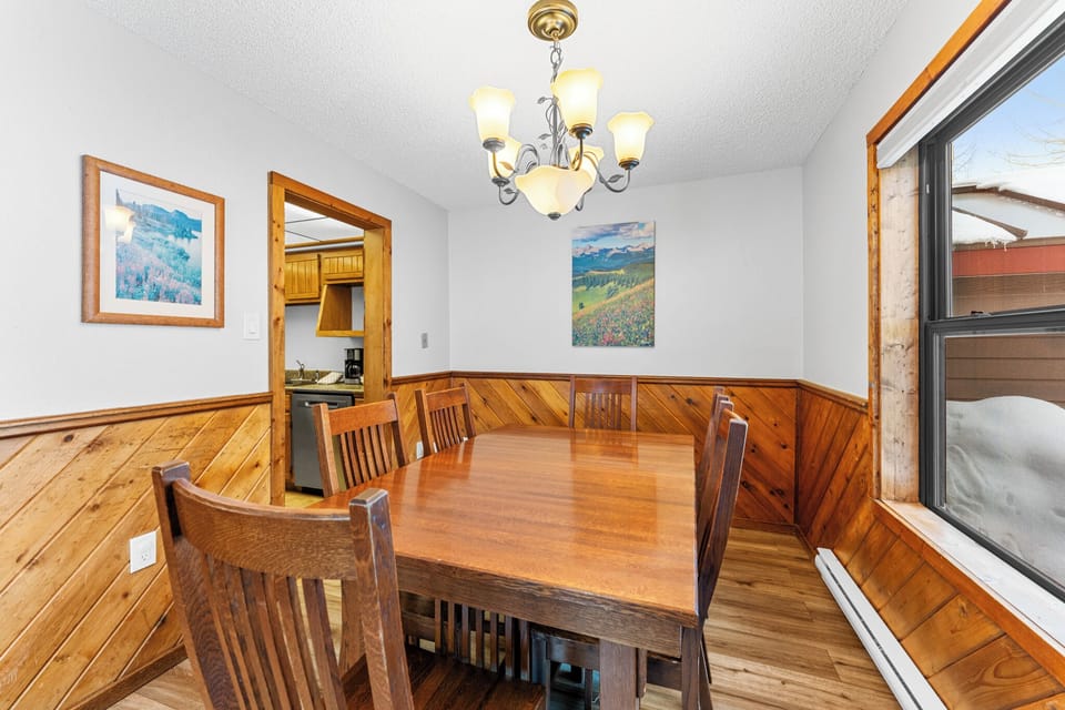 Gather around this warm wooden dining table under elegant chandelier light, where mountain views and cozy wood paneling create the perfect setting for your meals.