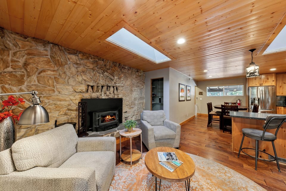 Cozy up by the stone fireplace in your warm living space, where wood ceilings and comfortable seating create the perfect mountain retreat atmosphere.