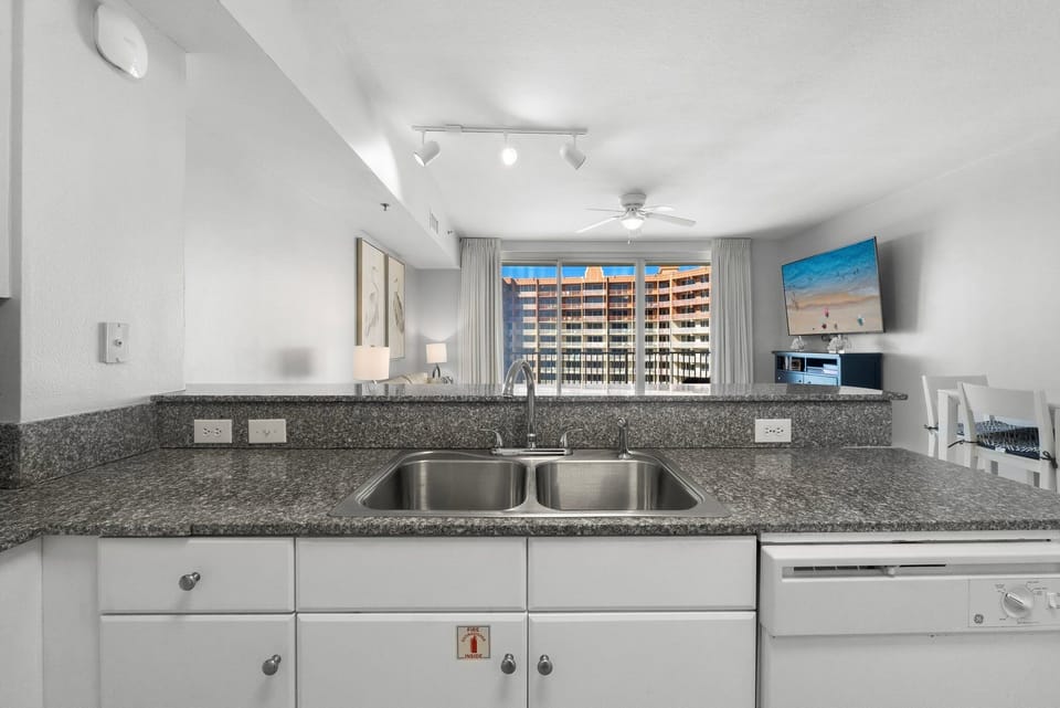 Modern kitchen with granite countertops and a view of the living area and balcony.