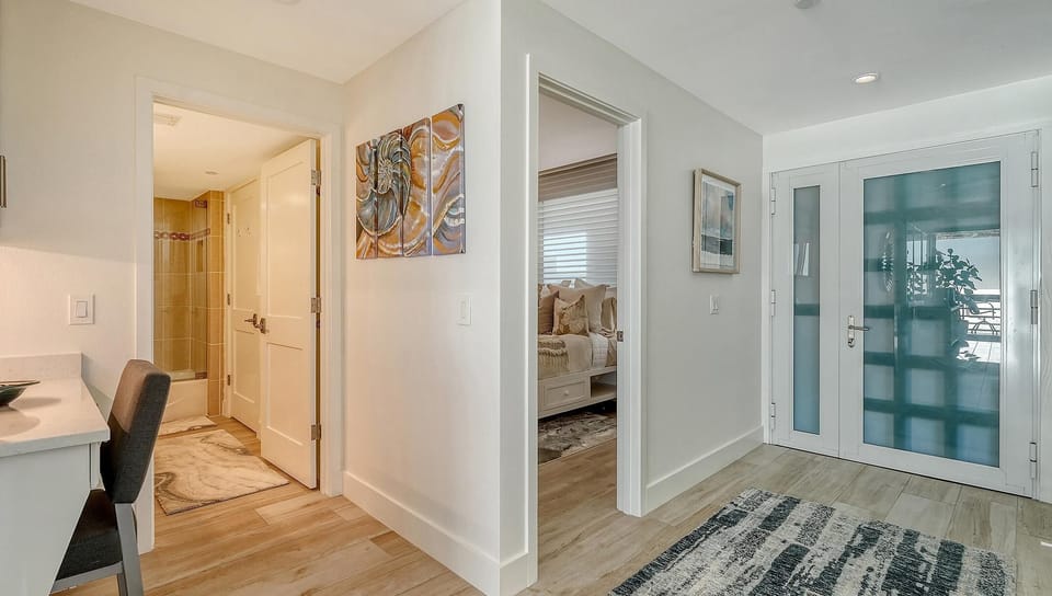 Entryway with frosted glass double doors, light wood flooring, and wall art leading to bedroom and bathroom.