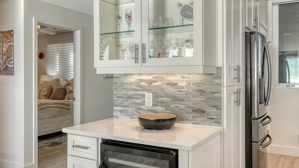 Kitchen corner with quartz countertop, gray geometric tile backsplash, glass-front cabinets, and stainless steel refrigerator.
