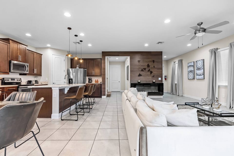 Experience a stylish living area that blends light and dark tones, centered around a modern white sofa. The warm wooden cabinetry and sleek barstools enhance the inviting atmosphere, ideal for relaxation and socializing.