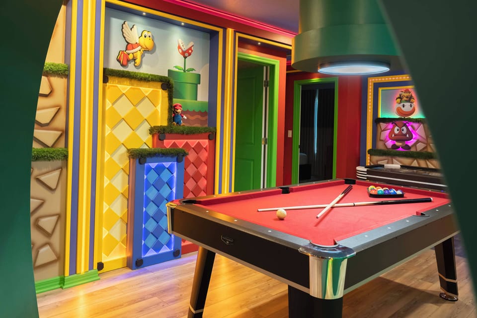 Enter a vibrant game room featuring a classic billiard table and playful murals inspired by retro video games. The warm wood flooring and bold walls set a lively atmosphere for friendly competition and laughter.