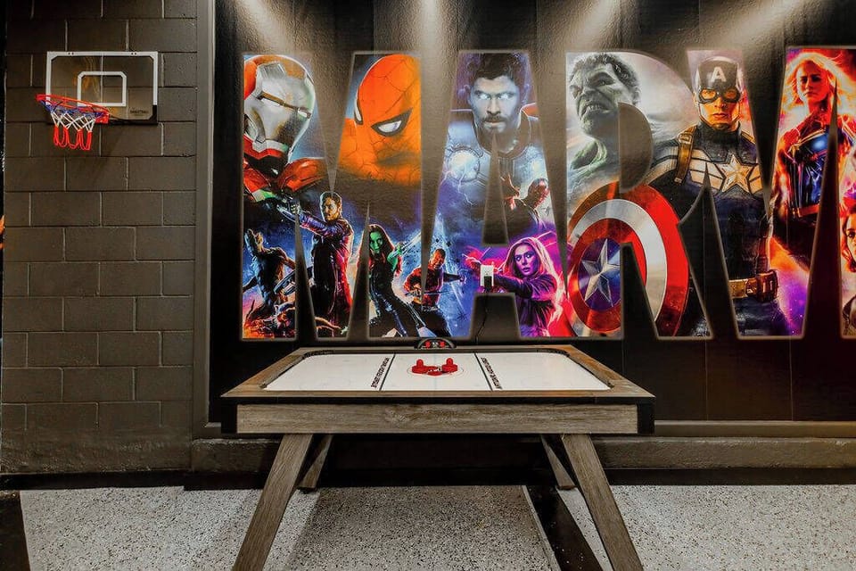 Step into a vibrant game room featuring a stunning mural of iconic superheroes, perfect for family fun or friendly competition. Enjoy the sleek air hockey table and a mini basketball hoop, all set against a stylish dark backdrop.