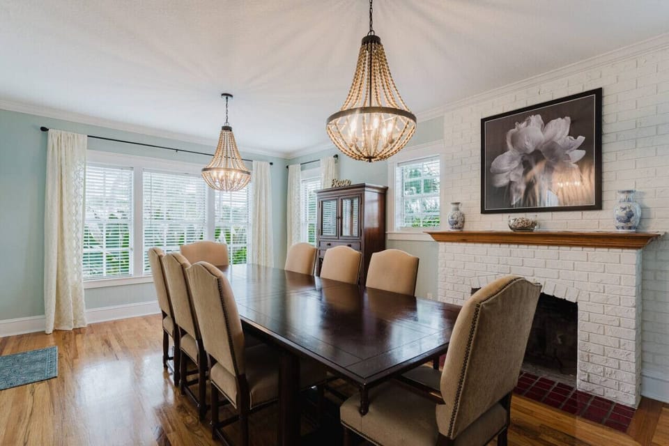 Enjoy a sunlit meal in this beautifully designed dining room, complete with cozy seating, elegant chandeliers, and a charming brick fireplace.