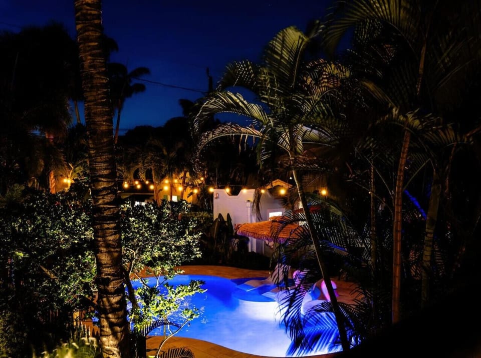 Bask in the enchanting glow of string lights by the pool, surrounded by lush palms for a magical evening retreat.