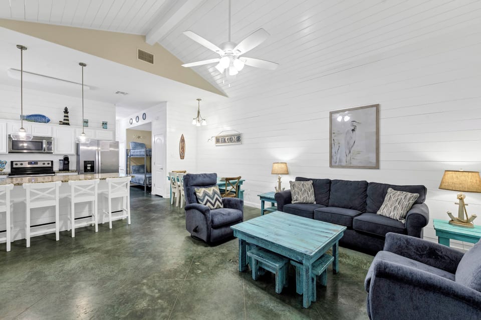 Relax in your coastal-themed living space with navy sofas and turquoise accents, seamlessly flowing into the open kitchen.