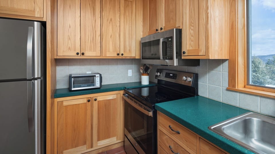 - Kitchen corner with microwave, oven, and wooden cabinetry   - Green countertop adds unique mountain cabin charm   - Fully stocked layout for cooking favorite family recipes