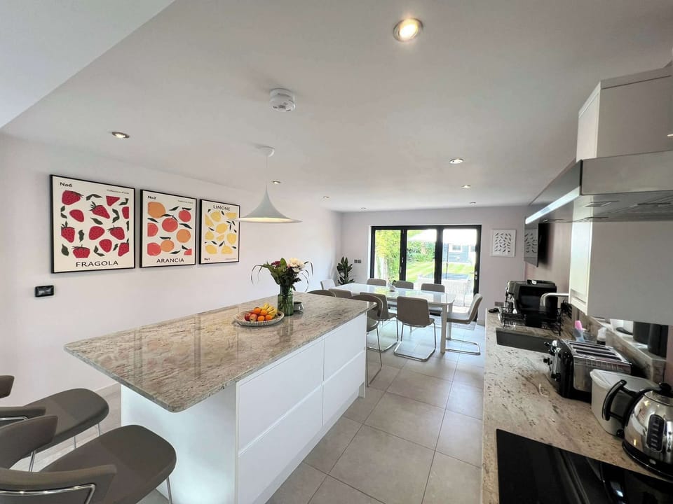 Open-plan kitchen with a central island offering bar stool seating for 4, and a dining table that seats 8. Amenities include American-style fridge freezer, oven, microwave, induction hob, high-end coffee machine, dishwasher, TV & underfloor heating.
