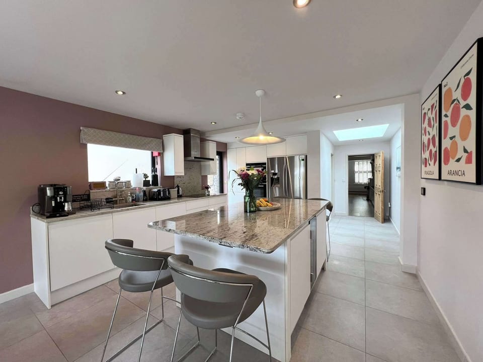 Open-plan kitchen with a central island offering bar stool seating for 4, and a dining table that seats 8. Amenities include American-style fridge freezer, oven, microwave, induction hob, high-end coffee machine, dishwasher, TV & underfloor heating.