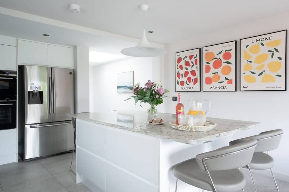 Open-plan kitchen with a central island offering bar stool seating for 4, and a dining table that seats 8. Amenities include American-style fridge freezer, oven, microwave, induction hob, high-end coffee machine, dishwasher, TV & underfloor heating.