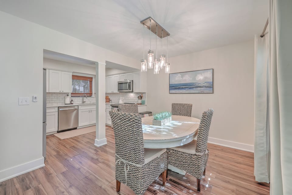 Gather for elegant meals at the dining table, beautifully lit by a modern chandelier and featuring comfortable wicker chairs.