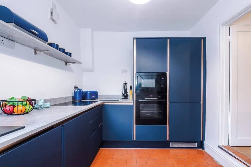 This cottage-style kitchen is modern and fully equipped, featuring bold blue cabinetry and tiled floors. It offers access to the backyard, creating a bright and functional space for cooking and entertaining.
