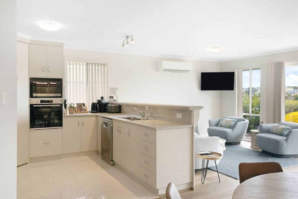 A modern, open-plan living space that combines a kitchen and a living area. The kitchen features built-in appliances and ample storage, while the living area includes comfortable seating and a large window that allows natural light to flood the room. The 