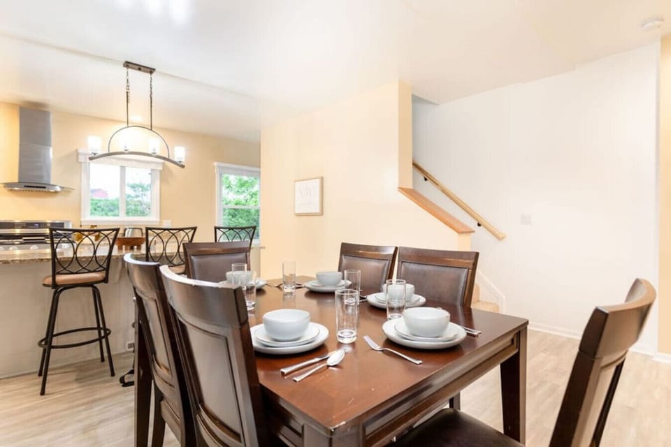 Dine together in the spacious dining area, featuring a dining table for six. Enjoy meals under modern lighting with views of the bright kitchen & barstool seating for three more at the island. Perfect for family dinners or entertaining friends.