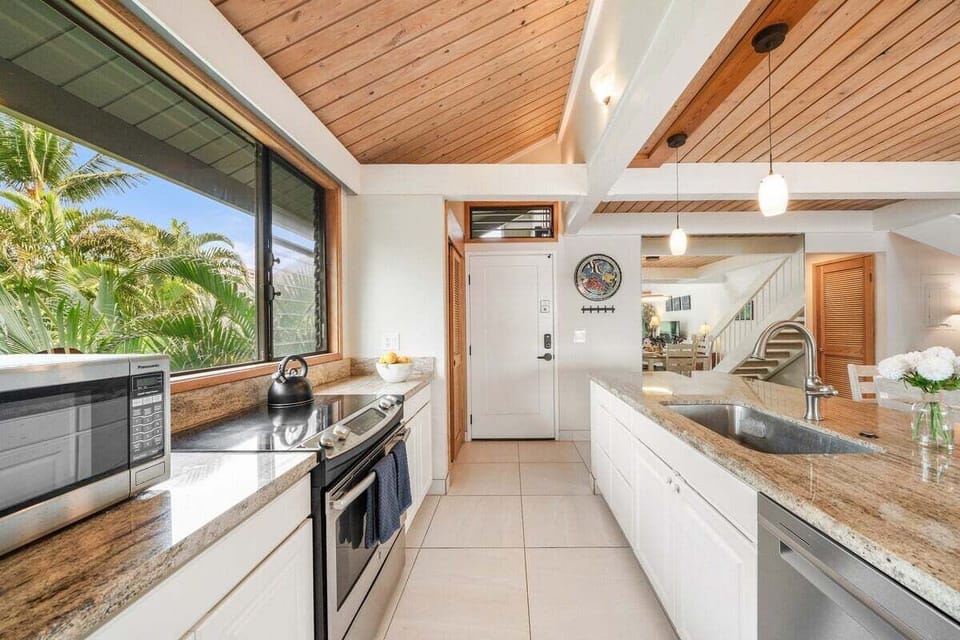 Bright kitchen with granite countertops, stainless steel appliances, and large windows overlooking tropical greenery