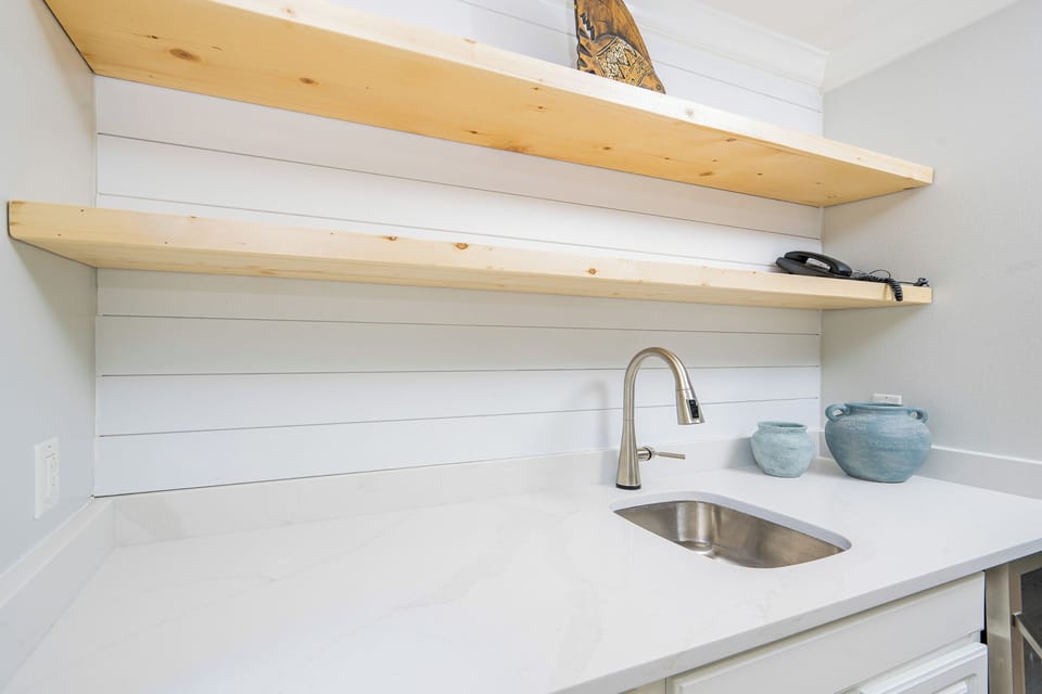 This wet bar features sleek white cabinetry, a stainless sink, and decorative blue vases, perfect for entertaining