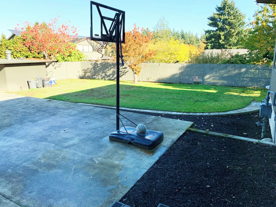 Backyard features a basketball hoop and spacious yard for play and relaxation.