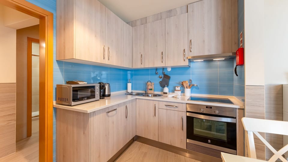 A fully equipped kitchenette featuring sleek appliances, a vibrant blue backsplash, and ample cabinet space for your culinary needs. #ModernKitchen #VacationRental