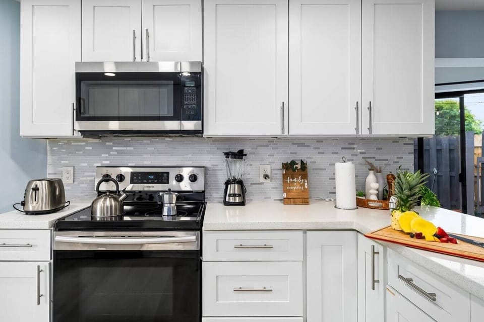 Modern fully equipped kitchen with stainless steel appliances, oven, microwave, toaster, blender, coffee maker, cookware, dishes, utensils, spacious countertops, and ample storage.