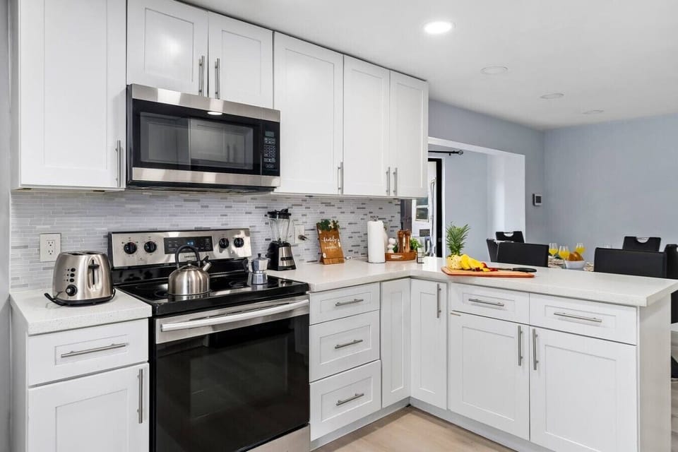 Modern fully equipped kitchen with stainless steel appliances, oven, microwave, toaster, blender, coffee maker, cookware, dishes, utensils, spacious countertops, and ample storage.