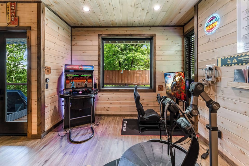 Game room with arcade machine, racing simulator, and virtual reality setup in a modern wood-paneled space.