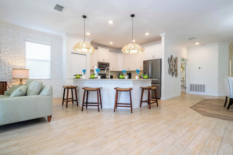 Sunlit living area with light wood-look floors, comfy sofa and airy coastal-modern styling-relax here after a day exploring Champions Gate or lounging by the pool.