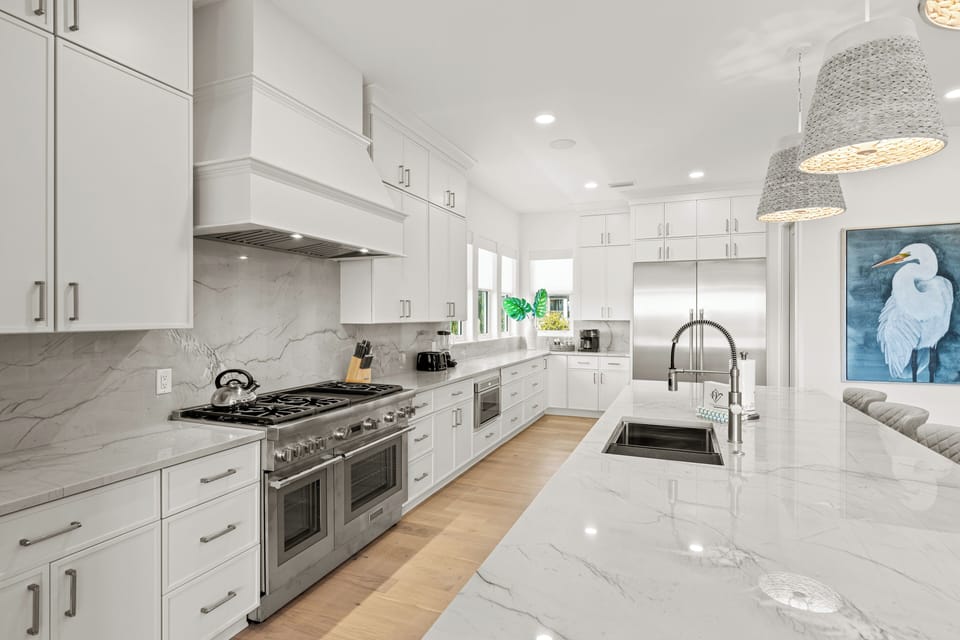 You'll love preparing meals in this elegant white kitchen with marble countertops, stainless steel appliances, and stylish pendant lighting.