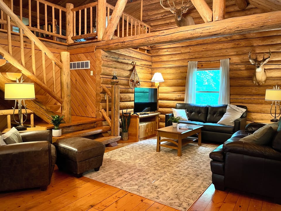 Cozy up in the rustic charm of Trillium Lane Cabin’s open-concept living room, featuring warm log interiors, inviting leather seating, nature-inspired decor, and a 50" Roku Smart TV for your entertainment