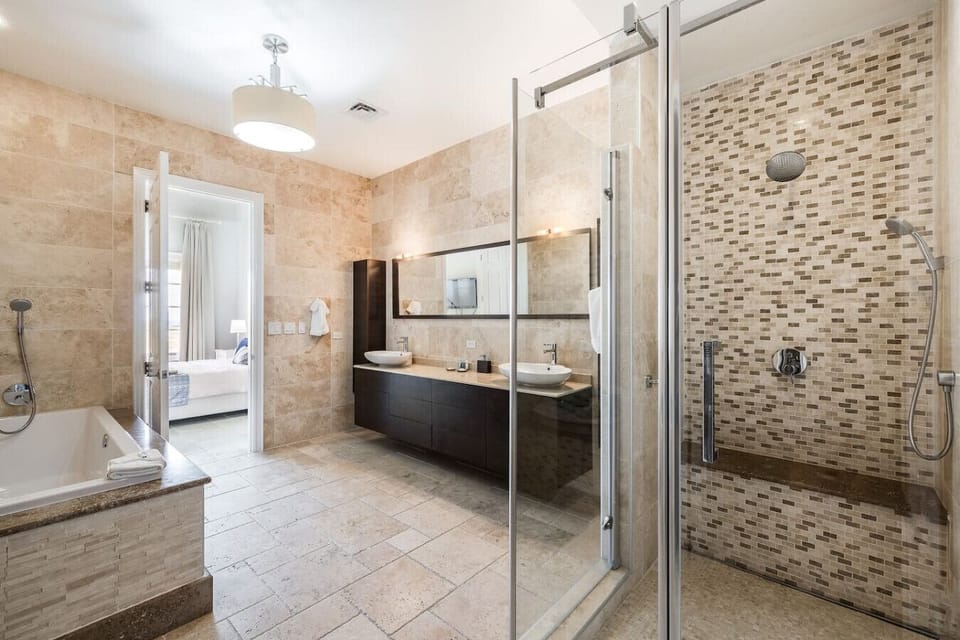 A spacious bathroom featuring a soaking tub, dual sinks, and a glass-enclosed shower with mosaic tile detailing, complemented by natural stone finishes.