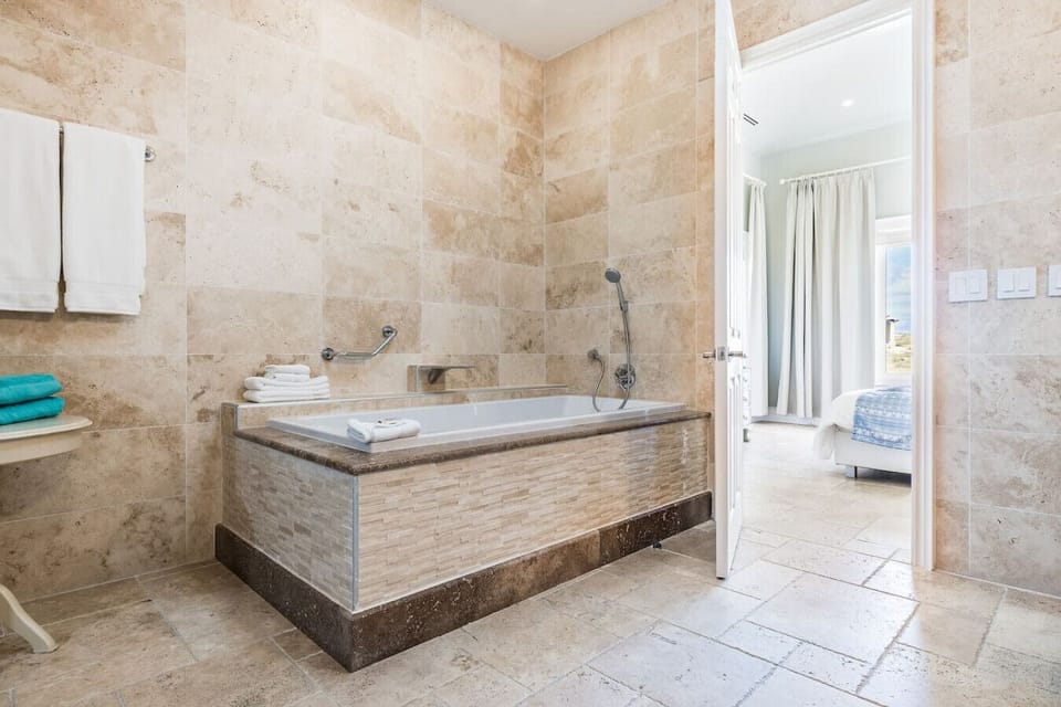 A spacious bathroom with a luxurious soaking tub, natural stone tiles, and fresh towels, offering a relaxing retreat.