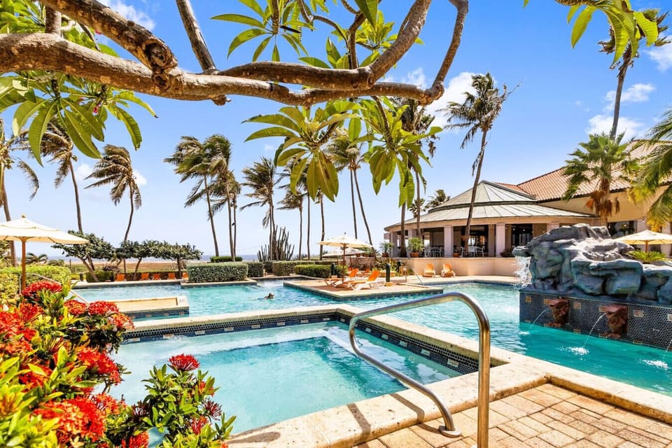A central water feature adds a serene touch with its gentle flow, while the adjacent sun loungers and umbrellas offer perfect spots for relaxation.