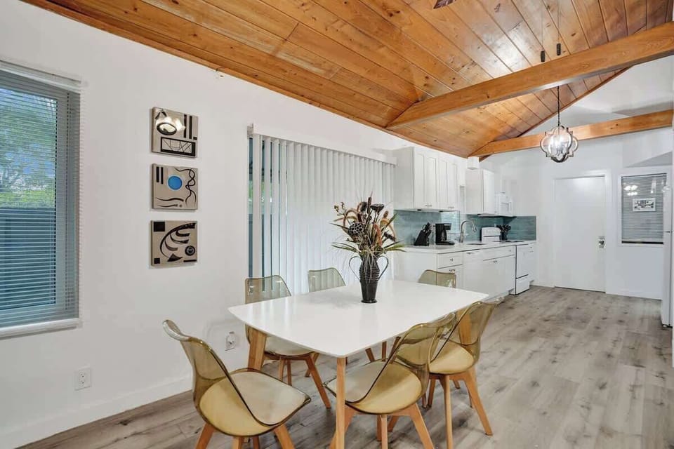 Dining table for six with pendant light, modern chairs, and open kitchen visible in the background.