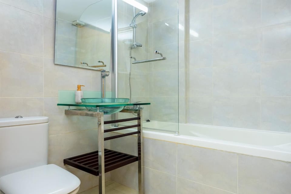 An interior view of a full bathroom, combining the glass elements from the previous restroom with a practical bathtub configuration.