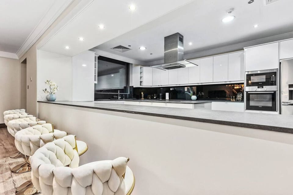 Sleek, modern kitchen with white cabinetry, black backsplash, and plush white bar stools.