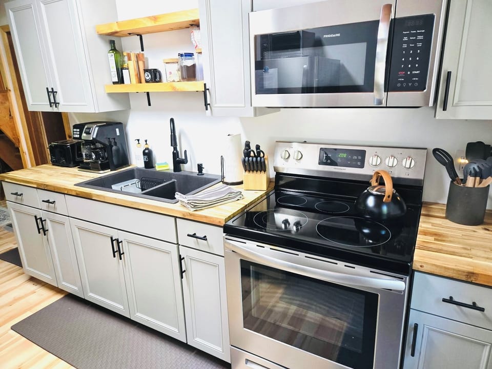 Galley kitchen with stove, microwave, refrigerator, toaster, dual coffee maker.