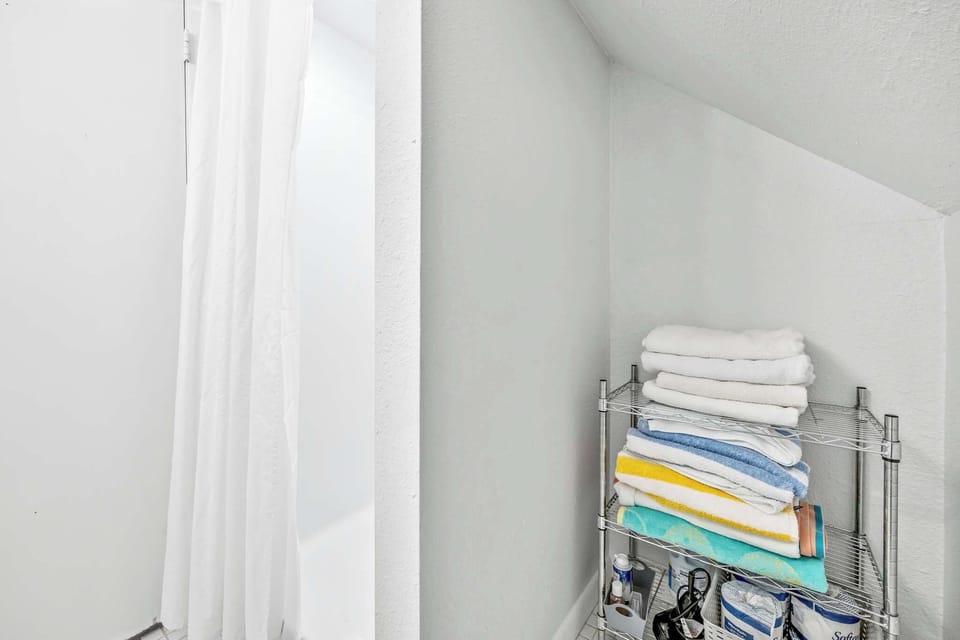 A neatly organized metal shelving unit stocked with fresh towels and bathroom essentials in a bright, white space.