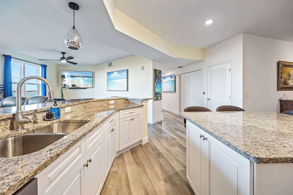 Modern kitchen with granite countertops and a view into the living area featuring coastal artwork.