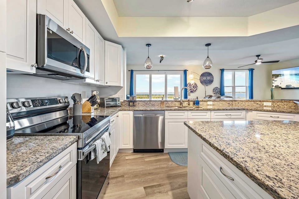 Modern kitchen with granite countertops and stainless steel appliances overlooking the living area.