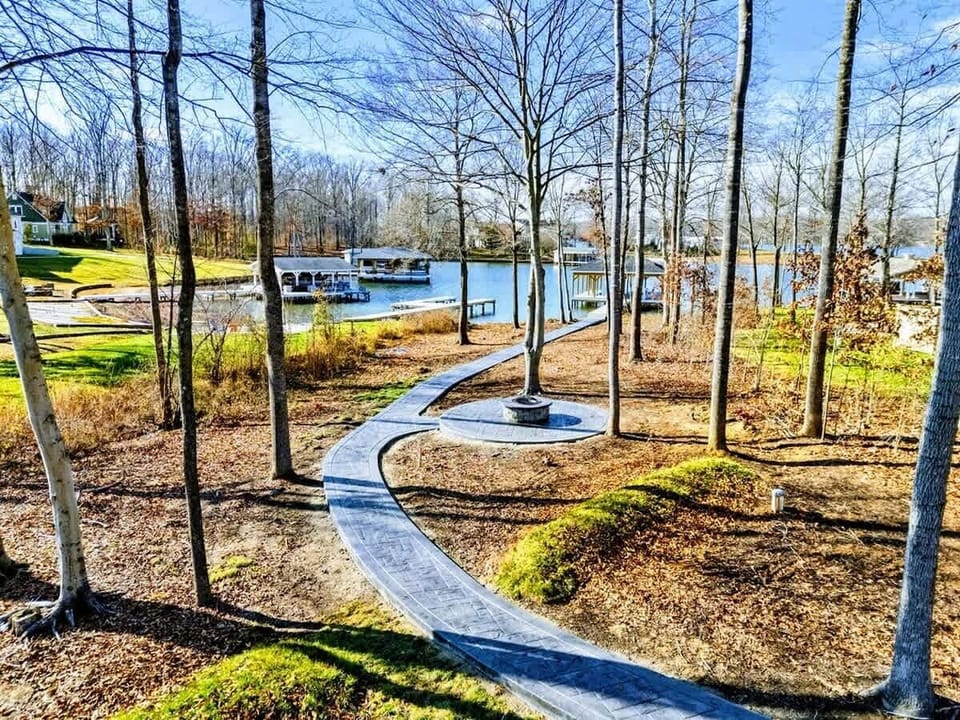 A picturesque outdoor fire pit with a paved walkway, surrounded by trees and offering stunning views of the lake.