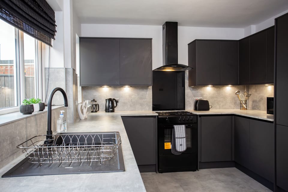 Cook in style in this sleek, modern kitchen featuring dark cabinetry, under-cabinet lighting, and all the essentials for a convenient and comfortable stay.