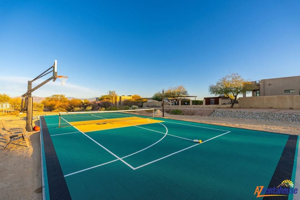 Private multi-sport court features basketball hoop and tennis net surrounded by desert landscape and modern architecture.