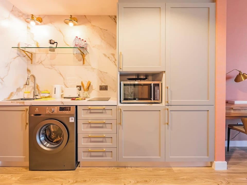 Stylish kitchenette with built-in fridge, washing machine, microwave, and essentials—perfect for light cooking and a comfortable stay.