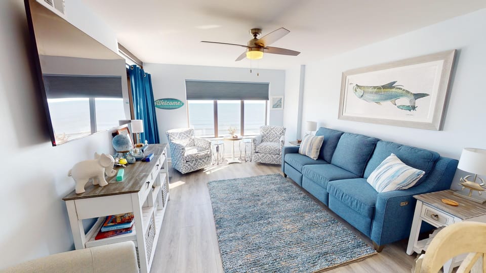 Living Area - Spacious living room connected to the dining area with large windows and seating arranged to enjoy the ocean view and relax after a day at the beach.