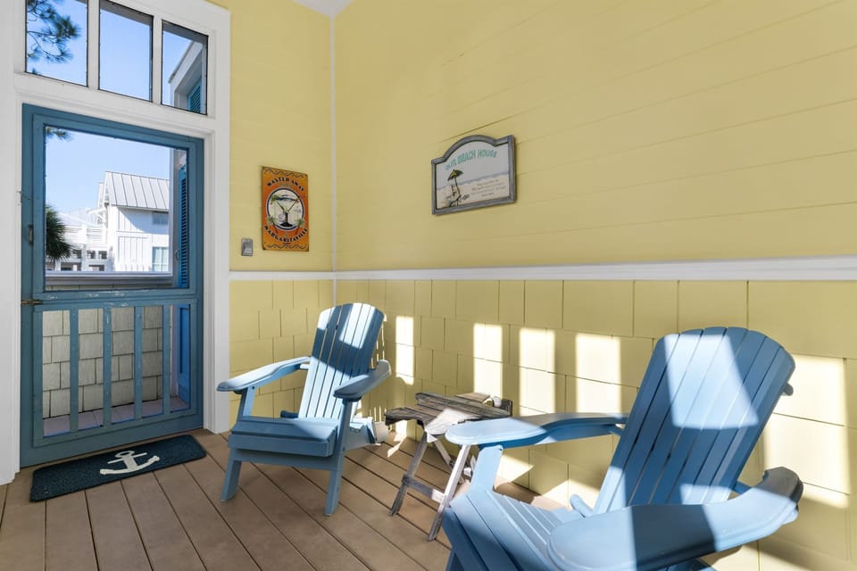 Settle into charming blue Adirondack chairs on your sunny enclosed porch, where warm yellow walls and peaceful views create your perfect morning coffee spot.
