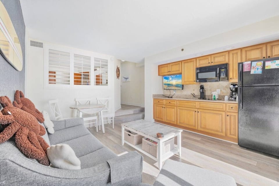 Fully stocked kitchen with modern appliances, dining area with seating for four, and living room featuring a sofa sleeper. Bright and open layout with stylish decor and ample natural light. Perfect for cooking, dining, and relaxing welcoming space.