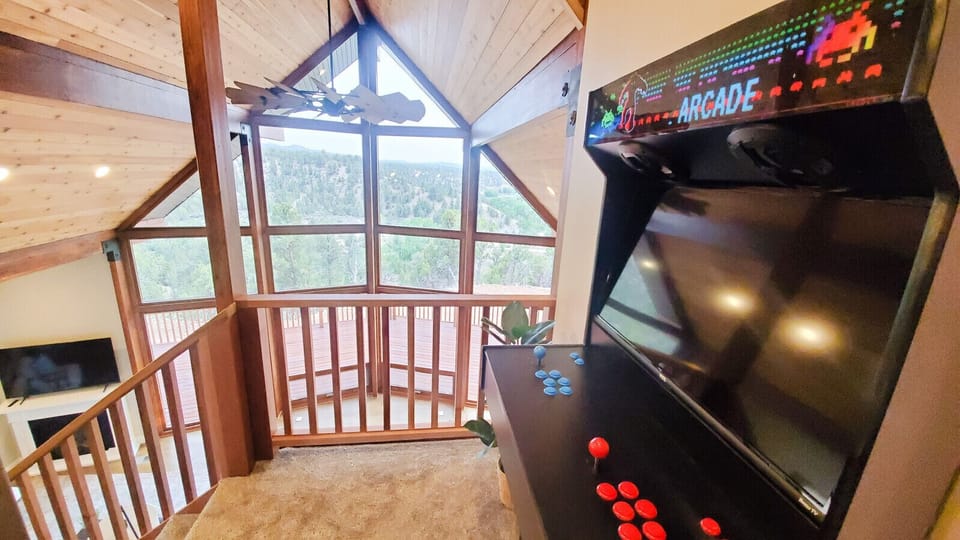 Fun loft area with an arcade game machine and stunning views of the forest through expansive windows.